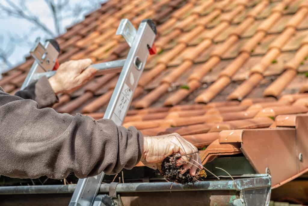 Man on a ladder cleaning house gutters